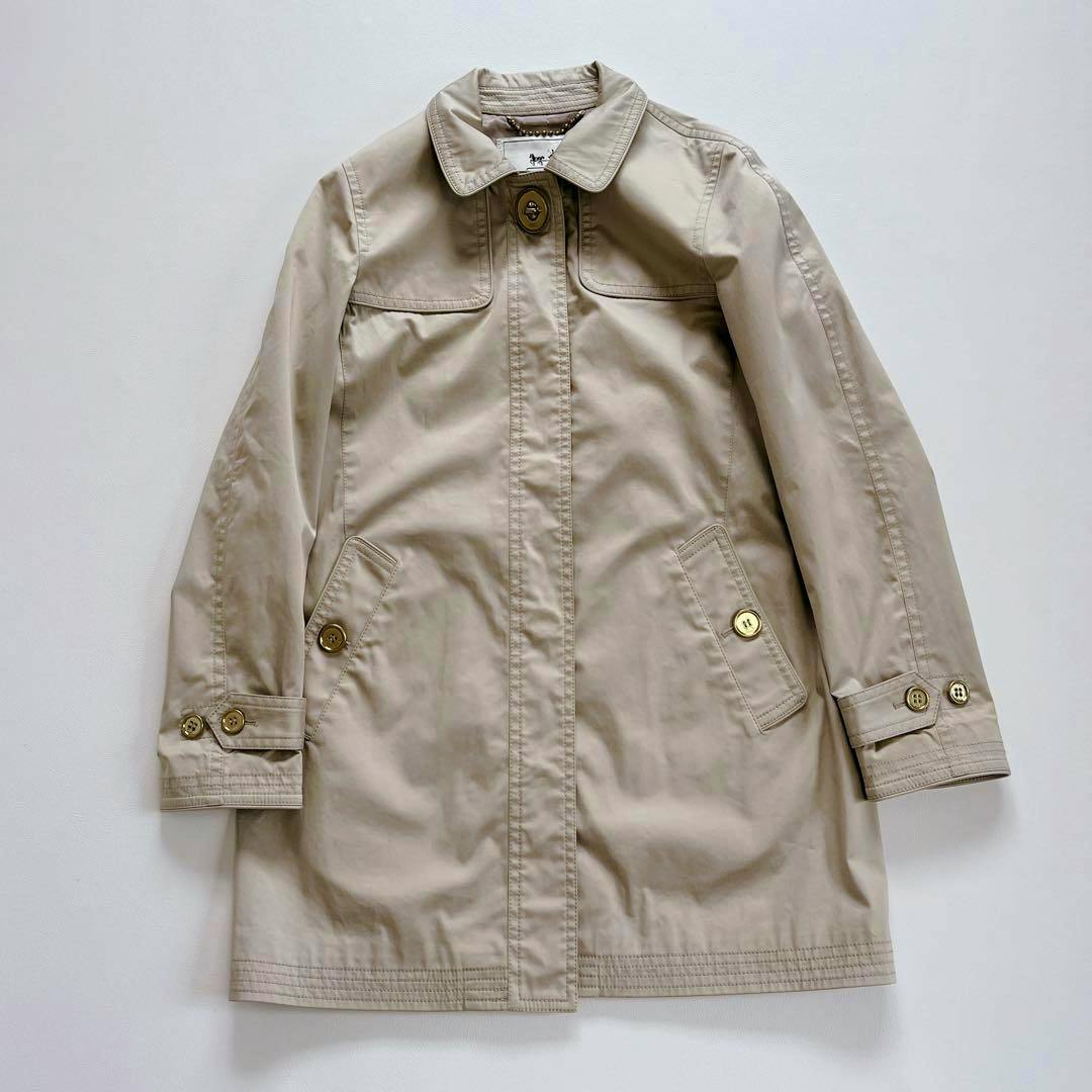 Beige Coach women's cotton jacket laid flat showing the front with button closure and flap pockets.
