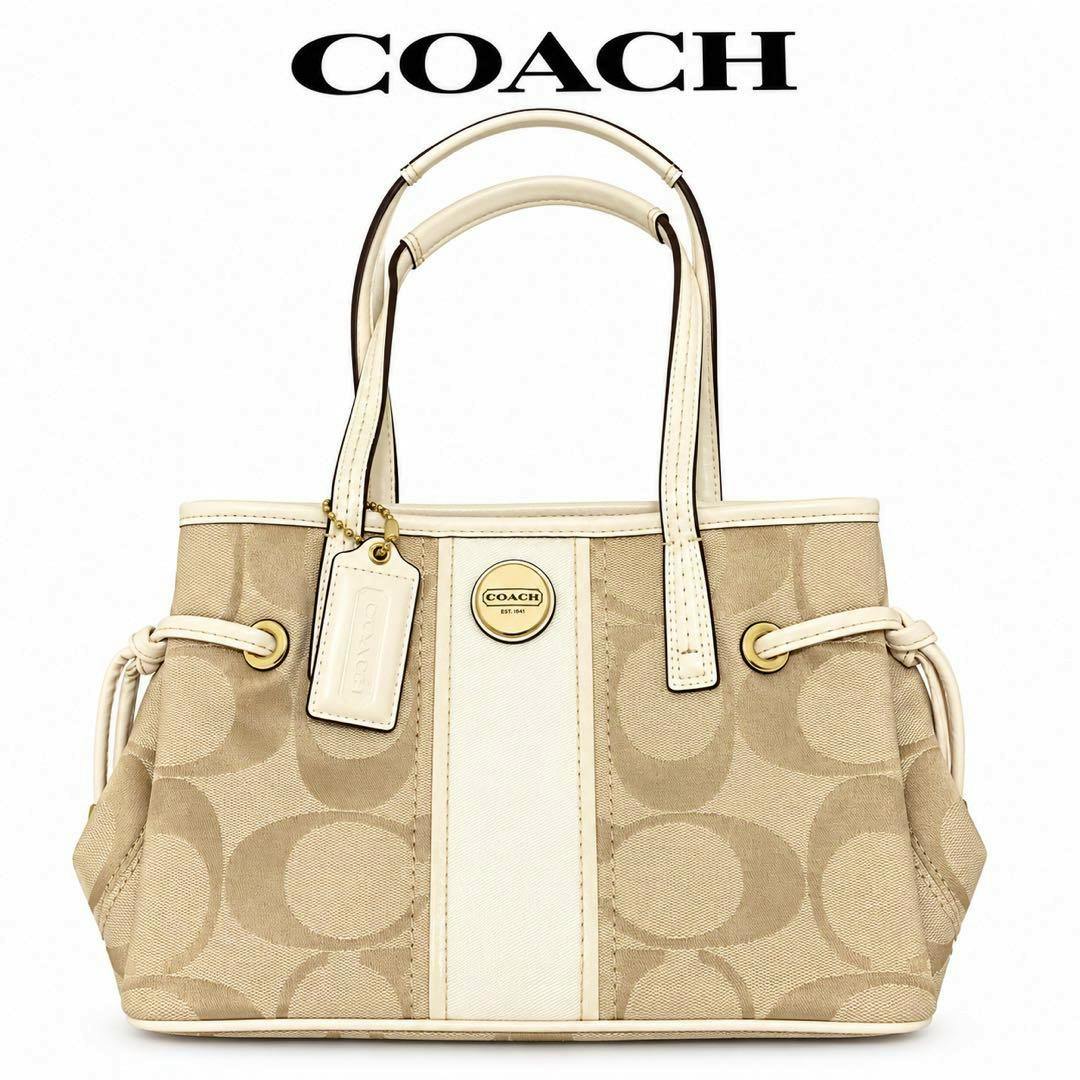 Beige Coach signature canvas tote bag with white center stripe, double handles, and hang tag on a white background.