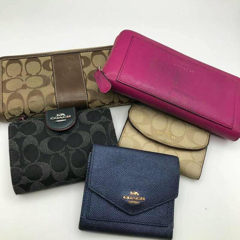 Five COACH wallets and a key case in various colors and canvas and leather finishes arranged on a white background.