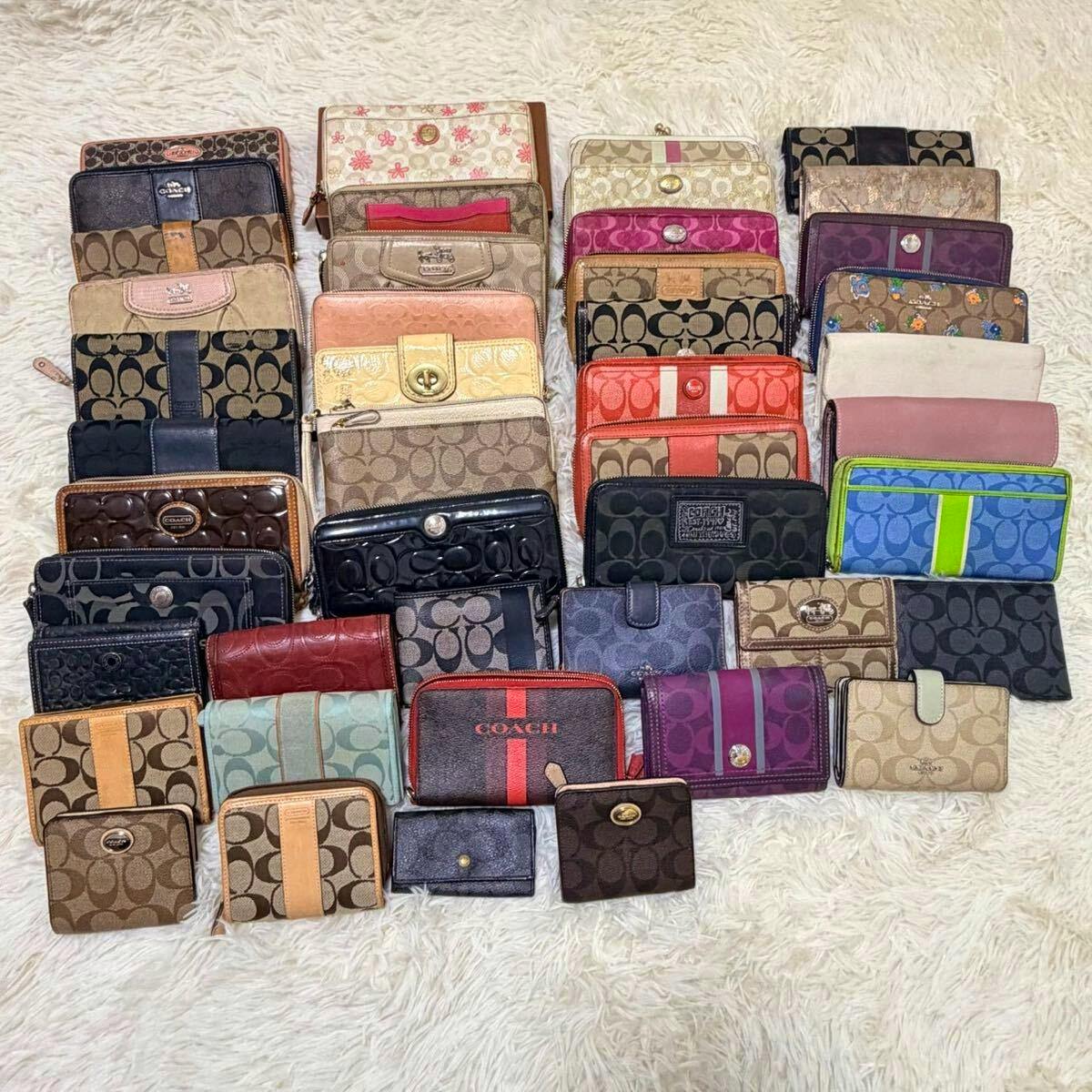 Multiple COACH wallets and small cases arranged in rows on a white shag rug, showing various colors and patterns.