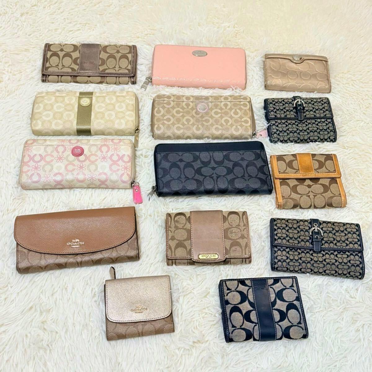 Several COACH wallets and key cases laid out on a white fuzzy surface, showing different signature monogram patterns and colors.