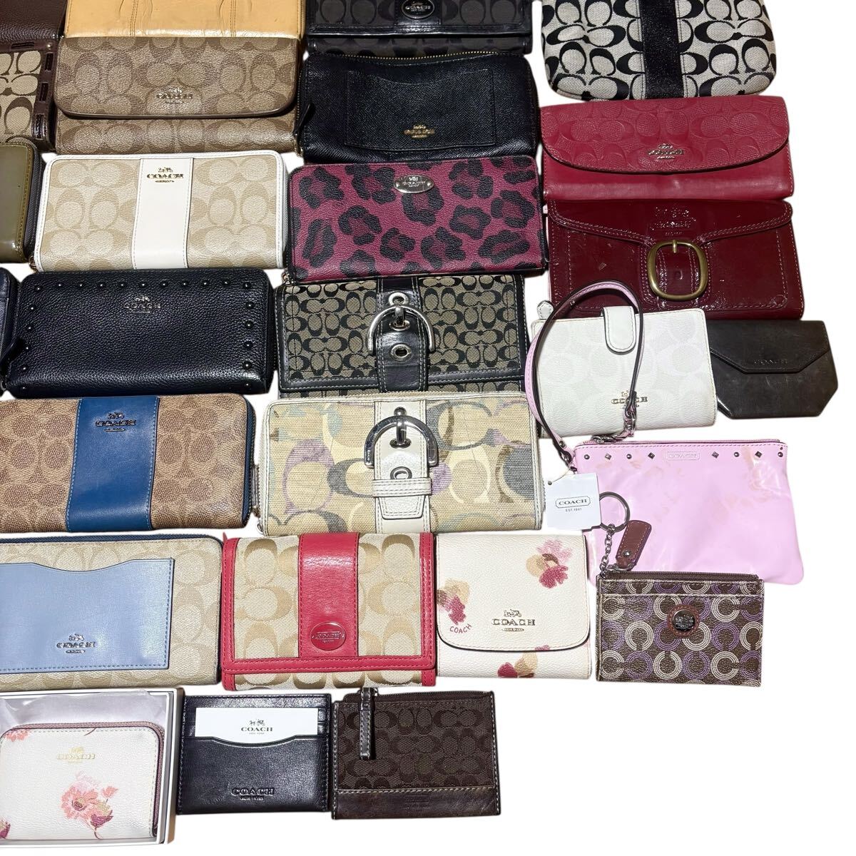 A collection of Coach wallets and small leather goods arranged flat in a grid, showing various colors and signature patterns.