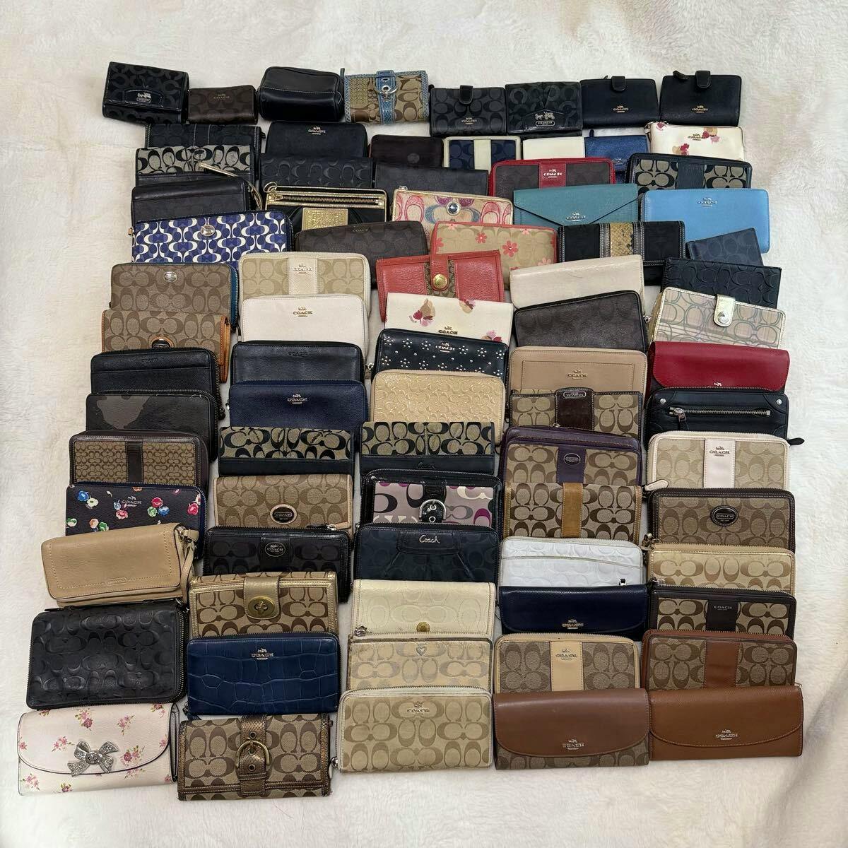 A large arranged set of Coach wallets and small leather goods laid out in rows on a light surface, showing assorted colors and signature patterns.