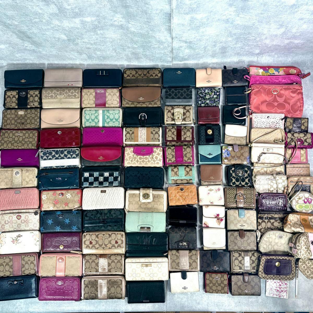 A flat lay of many Coach wallets, coin purses, and small pouches arranged in a grid on a light background.