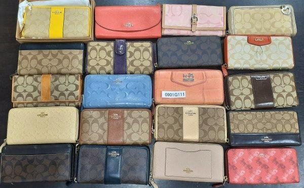 Multiple Coach wallets and small pouches arranged in rows on a flat surface, showing assorted colors and canvas signature patterns.