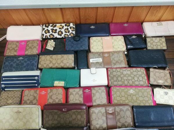 A collection of used Coach wallets and coin purses arranged on a wooden surface, showing various colors and signature patterns.
