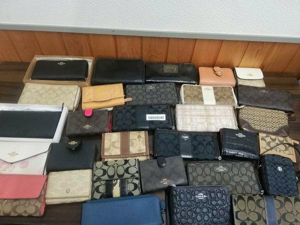 A collection of used COACH wallets and coin purses arranged on a table showing various patterns, colors, and an item number card.
