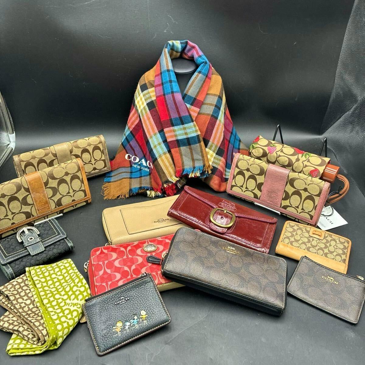 Multiple Coach wallets and small accessories, plus a plaid Coach scarf, arranged on a black background.