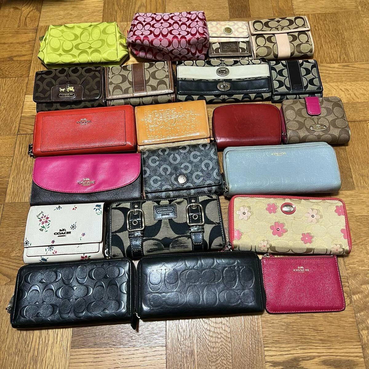 A laid-out set of Coach wallets and small pouches in various colors and signature patterns arranged on a wooden floor.