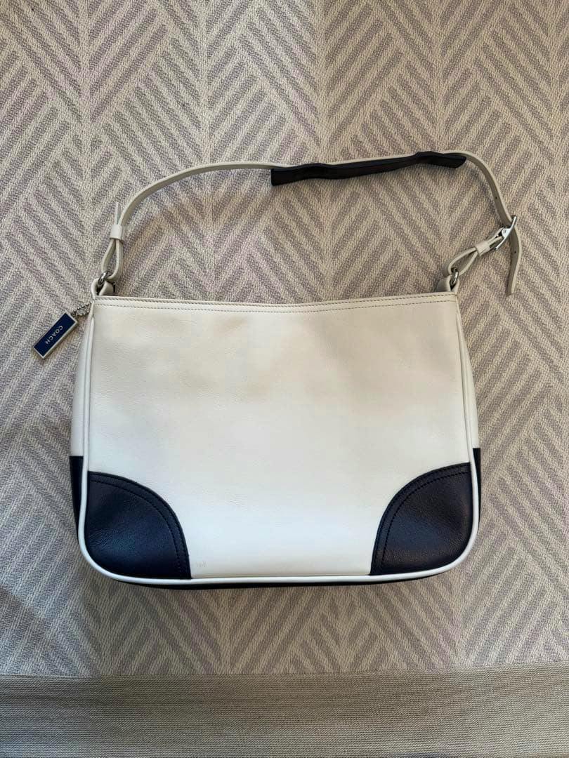 White and black Coach leather handbag laid flat showing the front, black corner accents, and shoulder strap.