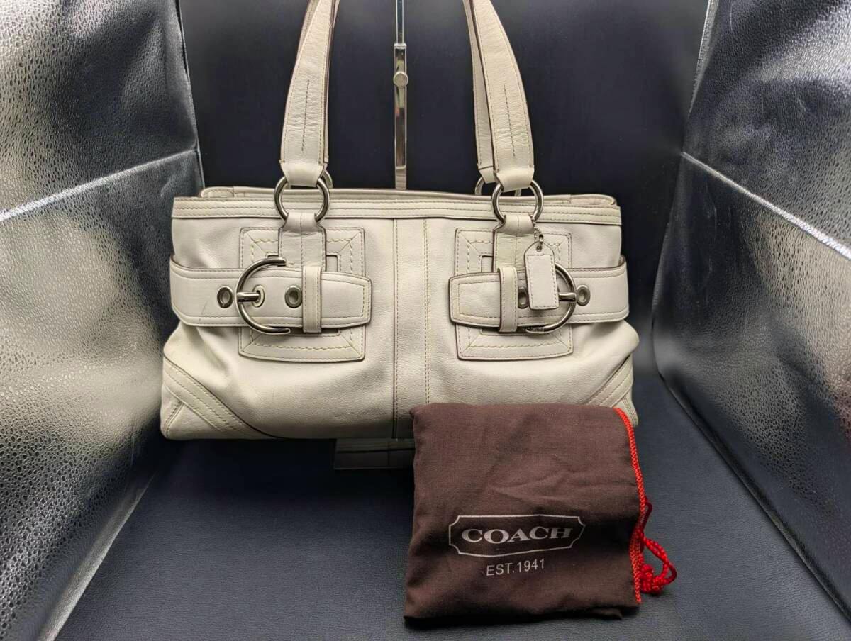 Front view of the COACH white leather handbag showing metal buckle details and a brown COACH drawstring dust bag in front.