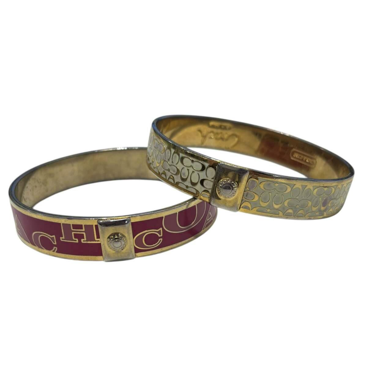 Two COACH bangle bracelets—one red with large COACH lettering and one gold-tone with signature C pattern—on a white background.