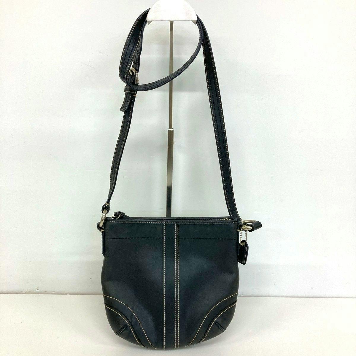 Black COACH shoulder bag with contrast stitching hanging from a display stand.