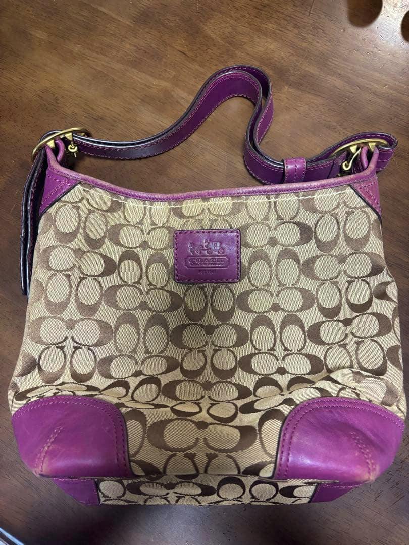 Canvas COACH women's bag with signature C pattern and purple leather trim lying on a wooden surface.