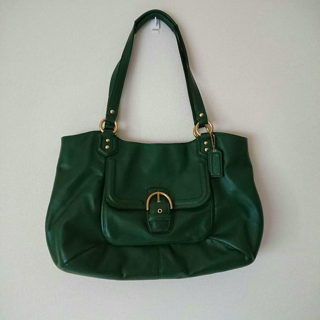 Green COACH cow leather women's shoulder bag with a front flap pocket and gold-tone hardware hanging on a wall.
