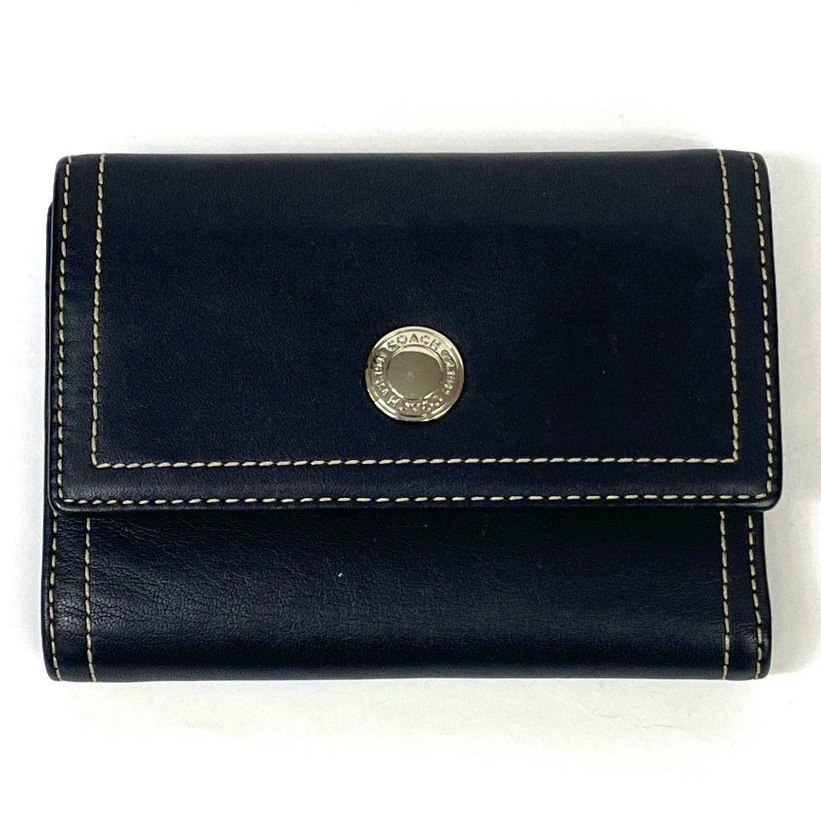 Black COACH three-fold cow leather wallet with cream contrast stitching and a round metal COACH snap on the front photographed on a white background.