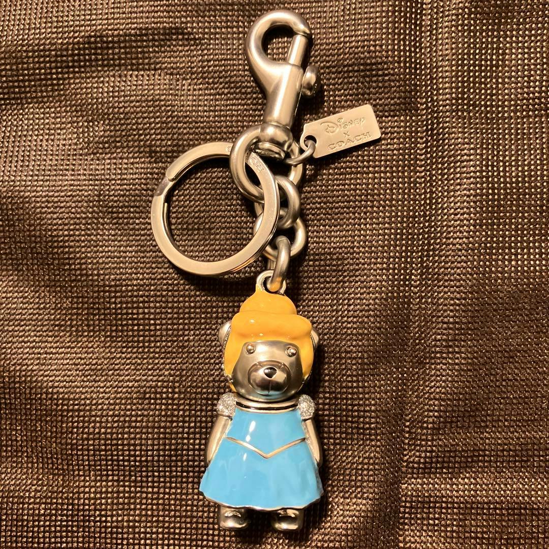 Front view of the Coach x Disney Cinderella zinc alloy bag charm showing the figure in a blue dress and yellow hair attached to a keyring and lobster clasp.