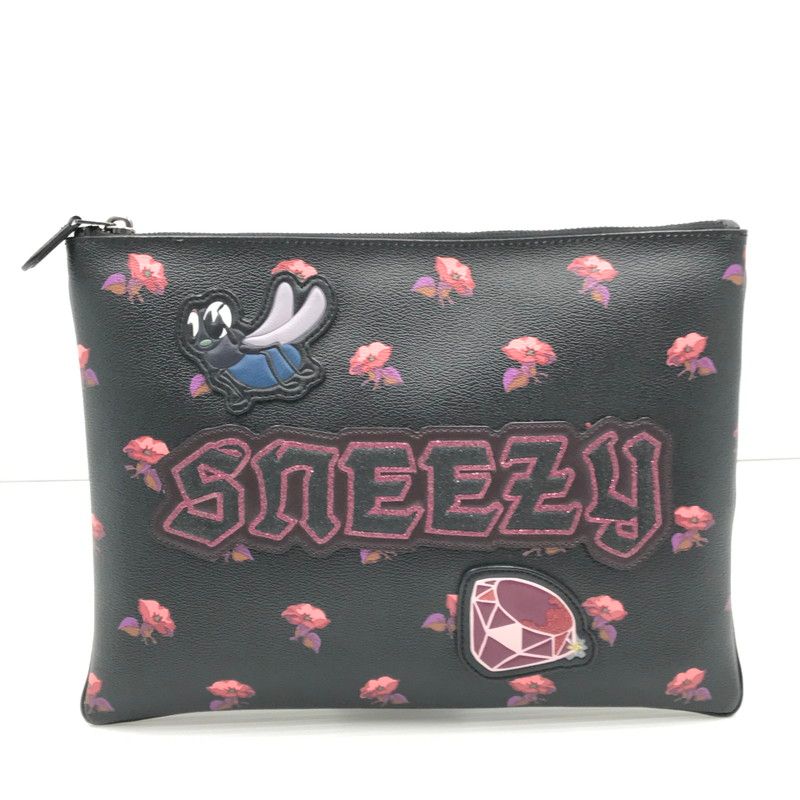Front view of the black COACH × DISNEY 'SNEEZY' cow leather clutch bag with small pink floral print, a character patch, and a gem patch.