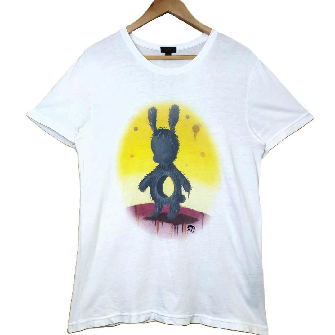 White cotton T-shirt with a Gary Baseman print of a furry rabbit-like character on a yellow background, shown hanging on a wooden hanger.