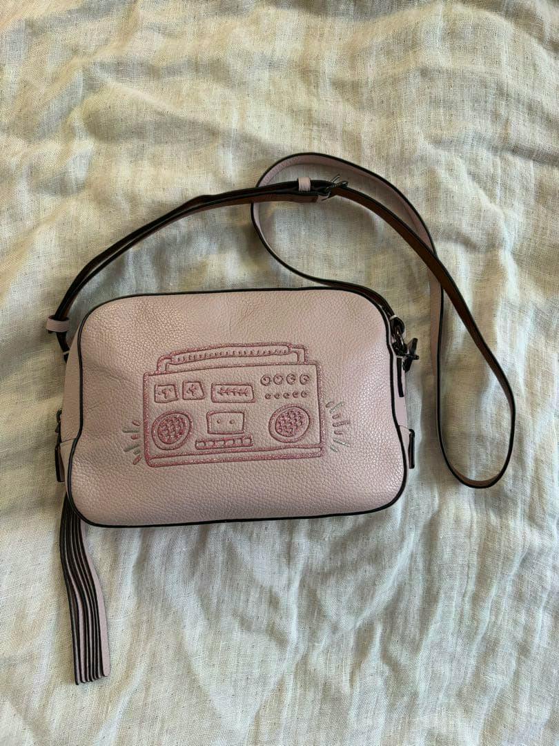Pink COACH shoulder bag with an embossed boombox design and long strap lying on a fabric surface.