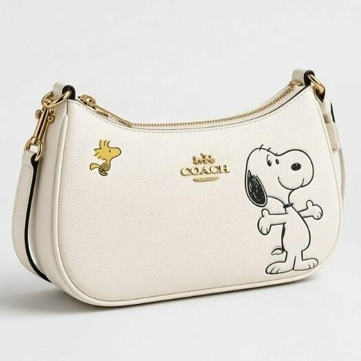 Front view of a white COACH Snoopy collaboration leather shoulder bag showing Snoopy and Woodstock prints and a gold Coach logo.