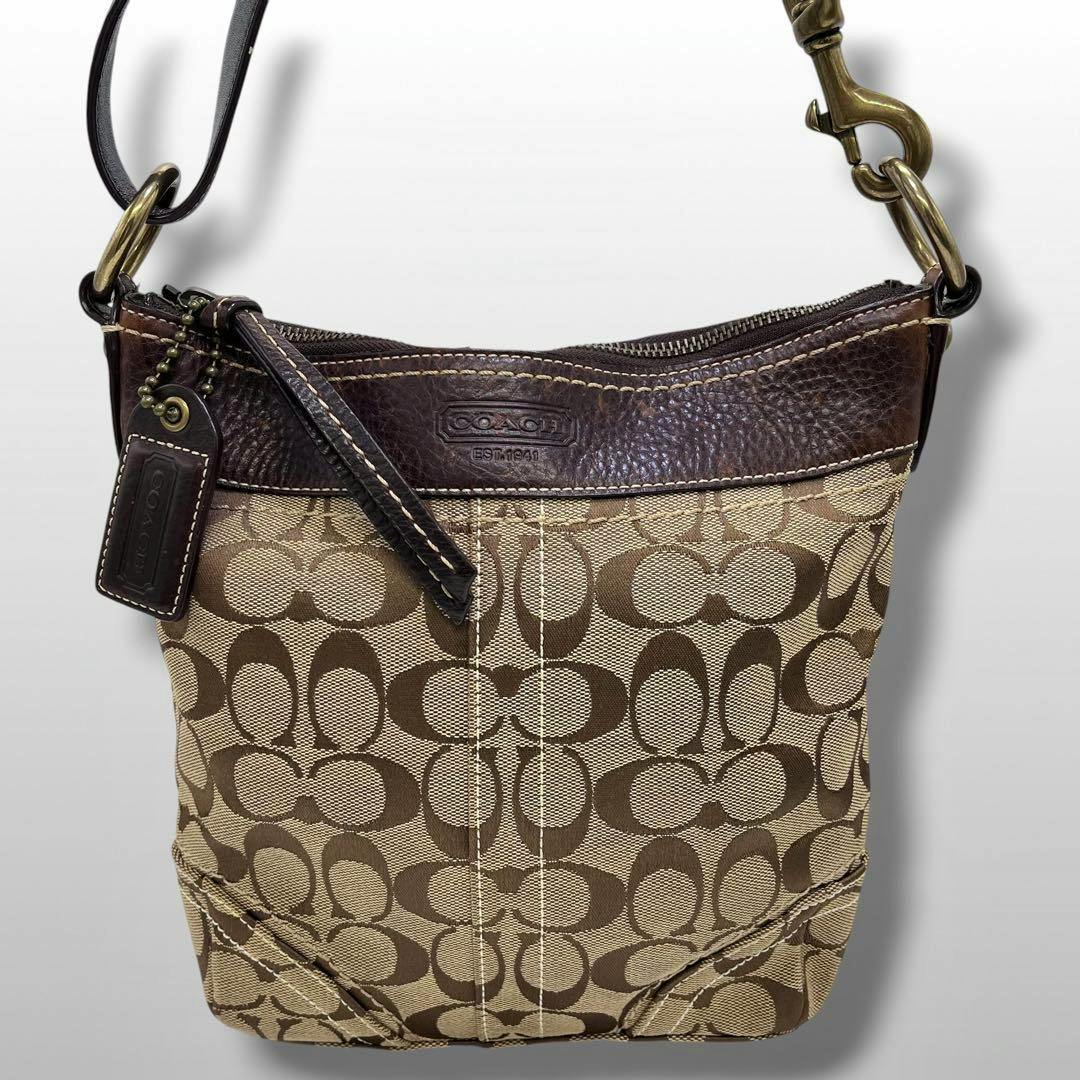 Front view of a COACH shoulder bag in brown signature canvas with dark leather trim and a leather hang tag.