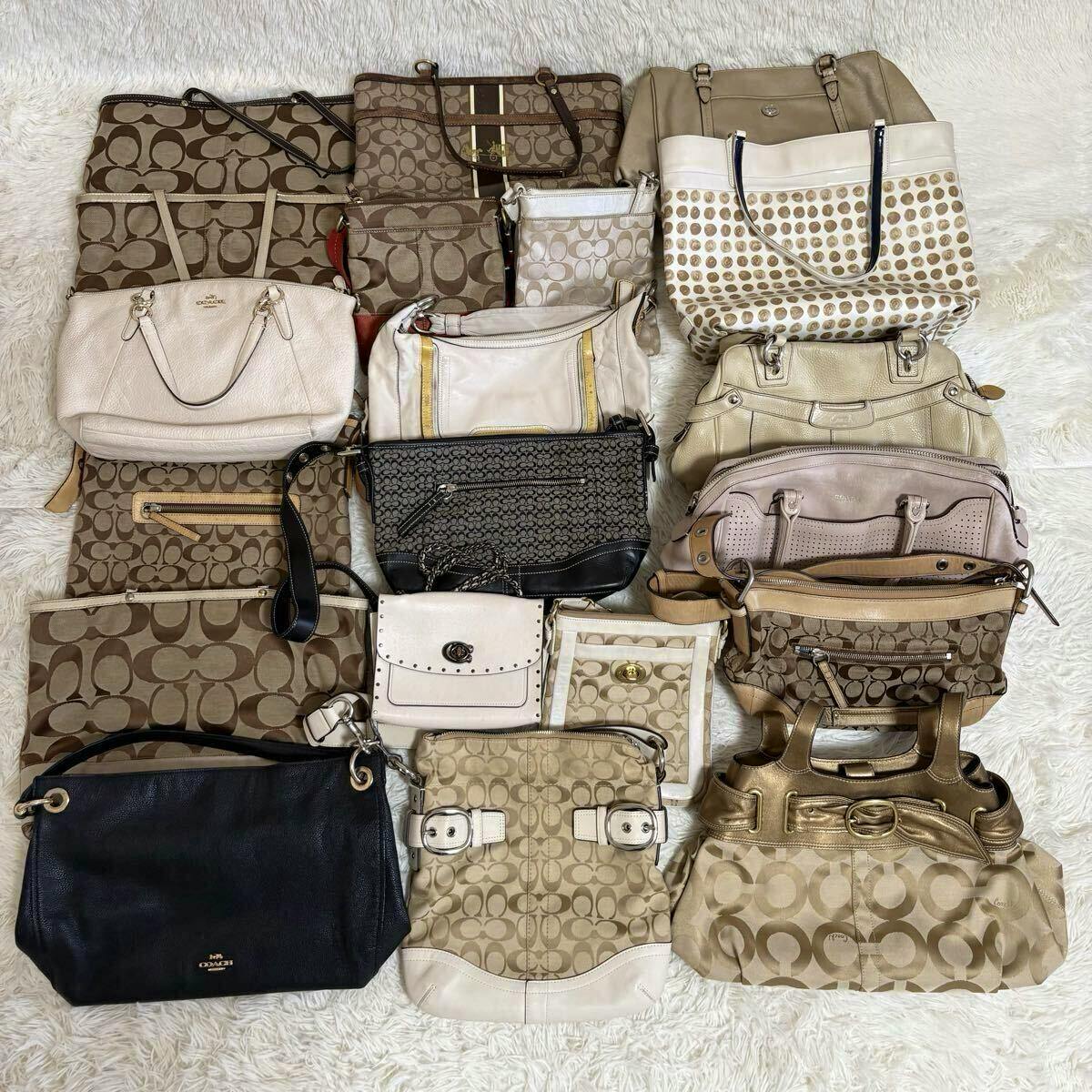 Multiple COACH canvas and leather bags arranged flat on a white rug, showing various tote, shoulder, and handbag styles with signature C patterns.