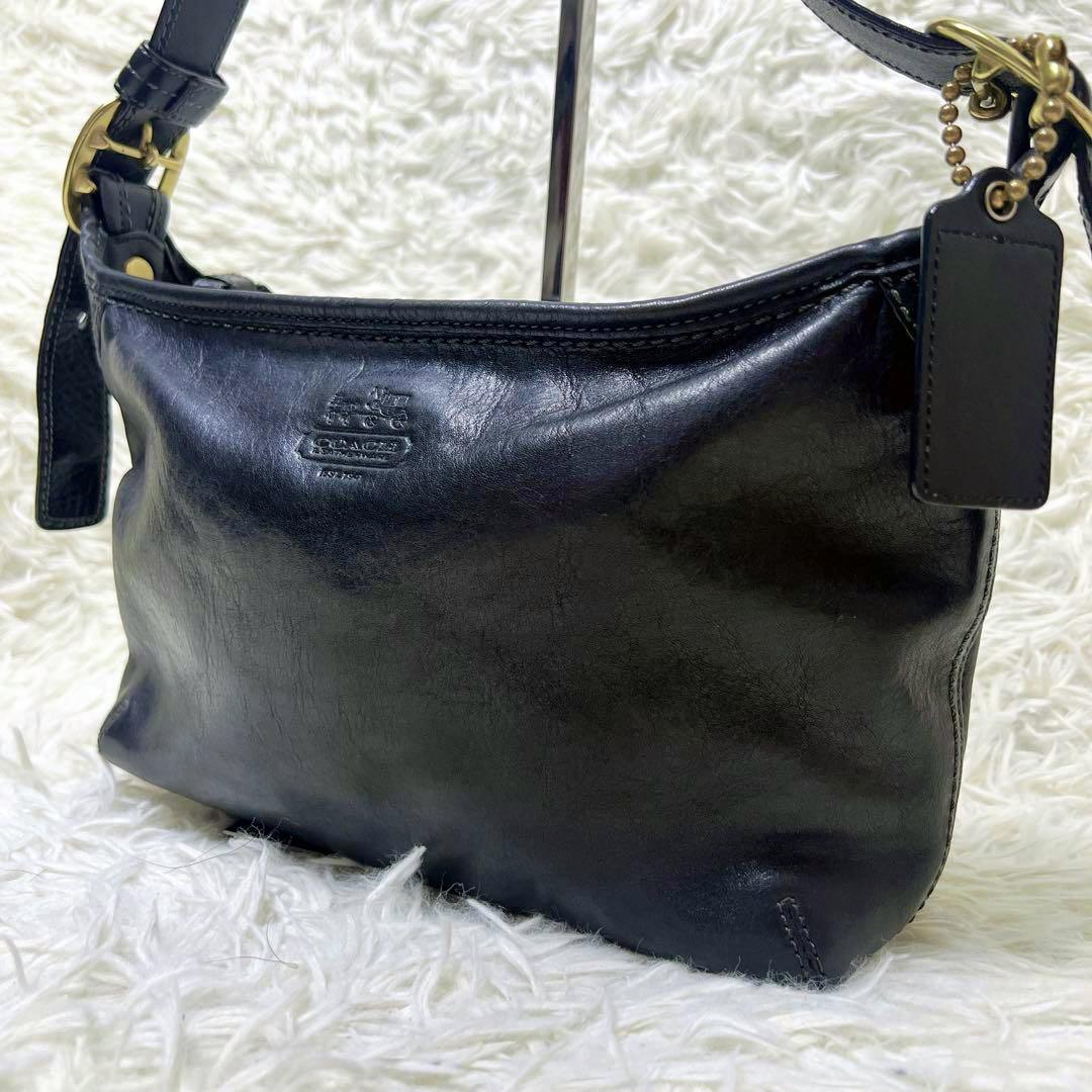 Front view of the COACH black leather Y2K shoulder bag with embossed logo and leather hang tag on a white shag background.