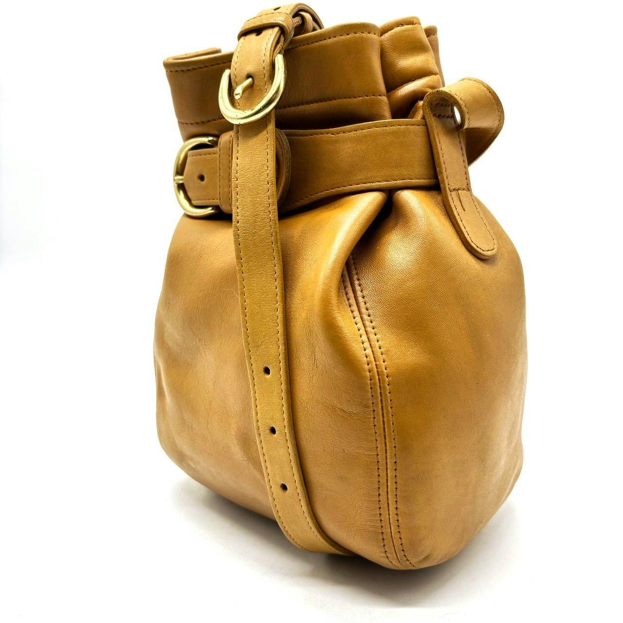 Side view of a camel leather Coach kinchaku shoulder bag showing strap and buckle.