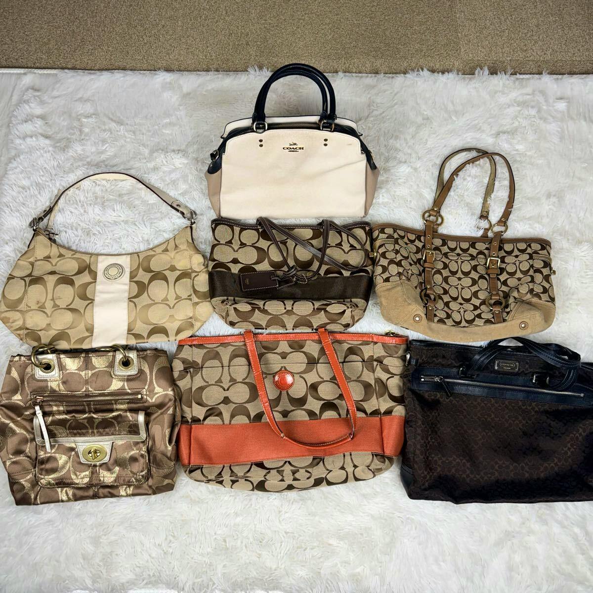 Seven Coach bags and pouches arranged on a white rug, showing various canvas styles and colors.