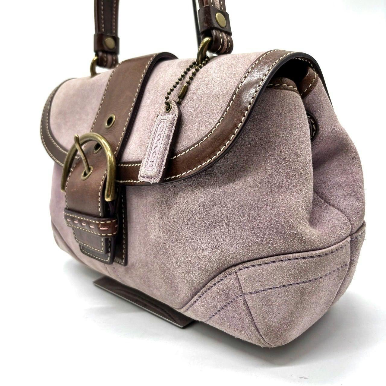 Close-up of a Coach pink-beige suede handbag with brown leather trim and brass hardware.