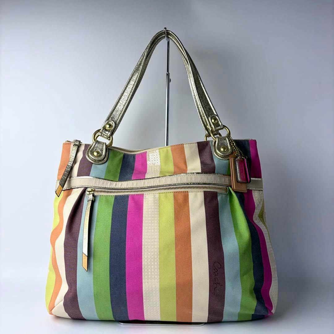 Front view of a Coach multicolor striped tote bag with metallic gold handles and a front zippered pocket.