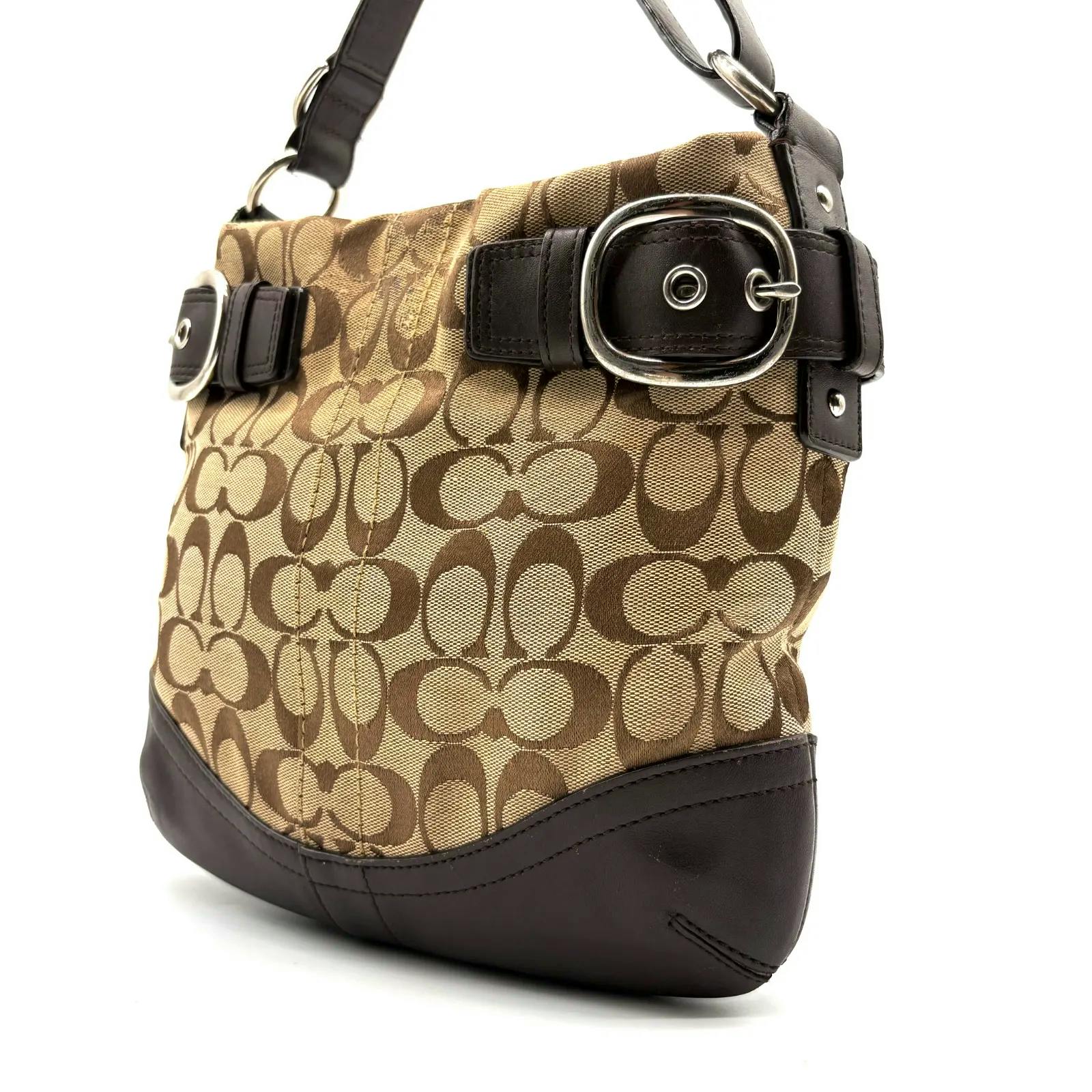 Close-up of the beige and dark brown COACH signature canvas shoulder bag showing leather trim, the bottom, and a silver buckle accent.