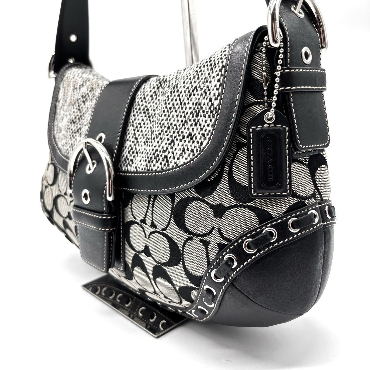Black and gray Coach signature canvas flap hobo shoulder bag with leather trim, buckle details, and a hanging leather tag.