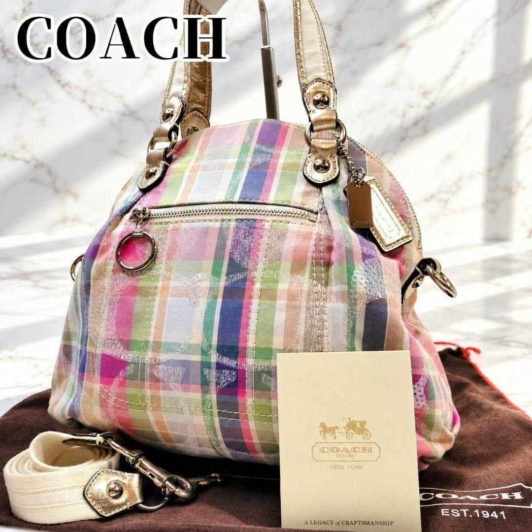 Front view of the COACH Madras check canvas shoulder bag with metallic handles and a detachable strap, shown with its booklet and dust bag.