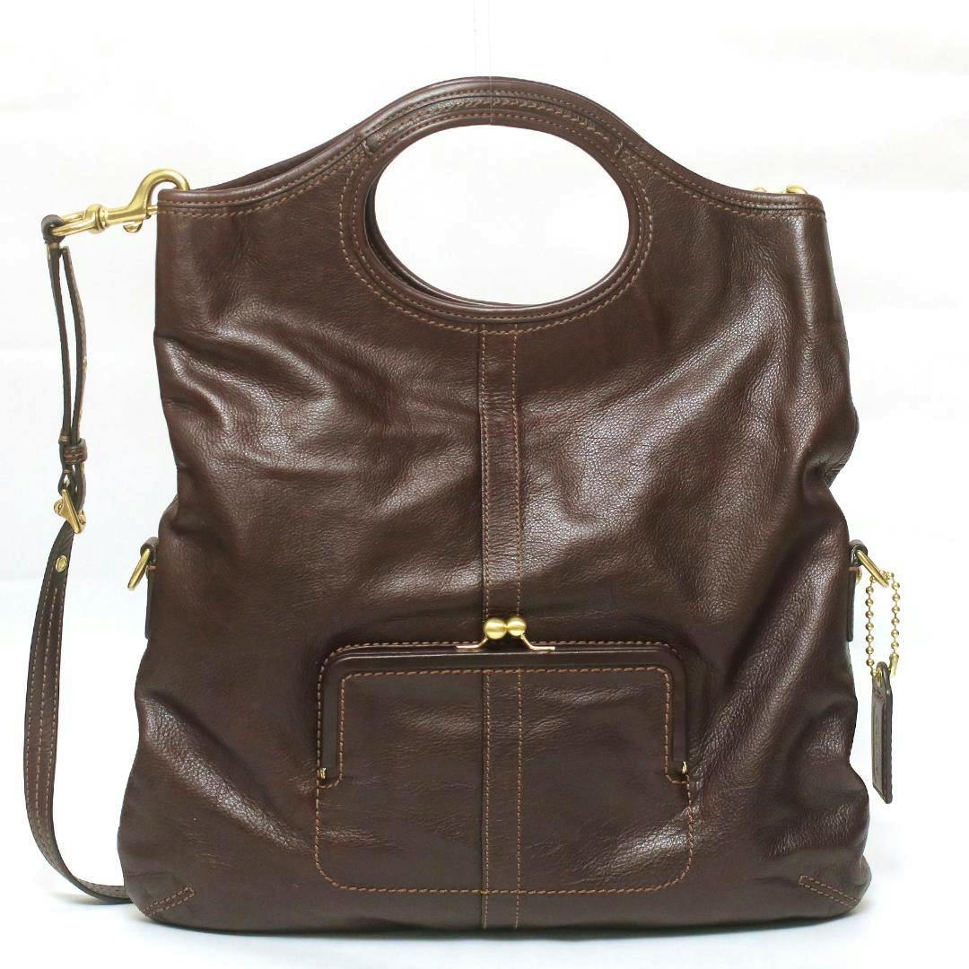 Front view of a brown cow leather Coach 2-way shoulder handbag with oval top handles, a front kiss-lock pocket, and a detachable shoulder strap.