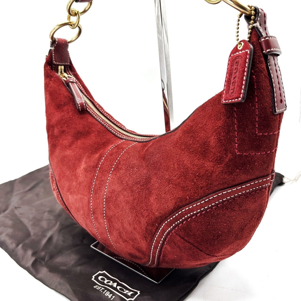 Red suede crescent Coach handbag with gold hardware and leather tag on a black dust bag.