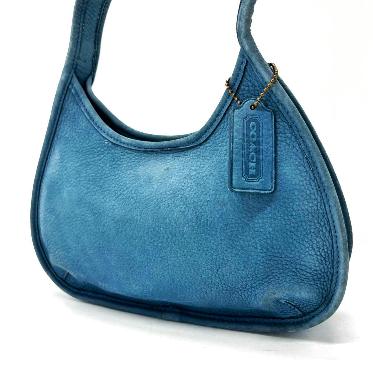 Front view of a blue Coach nubuck leather handbag with a hanging Coach tag.
