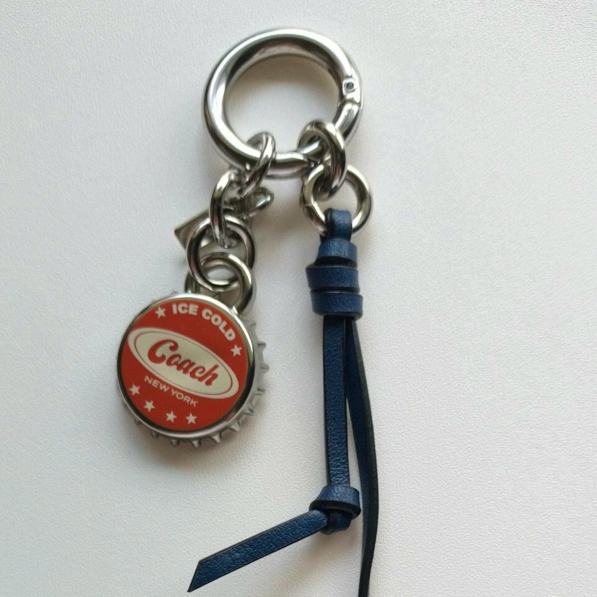 COACH bag charm keyring showing a silver ring with a red bottle-cap metal Coach medallion and a blue leather tassel.