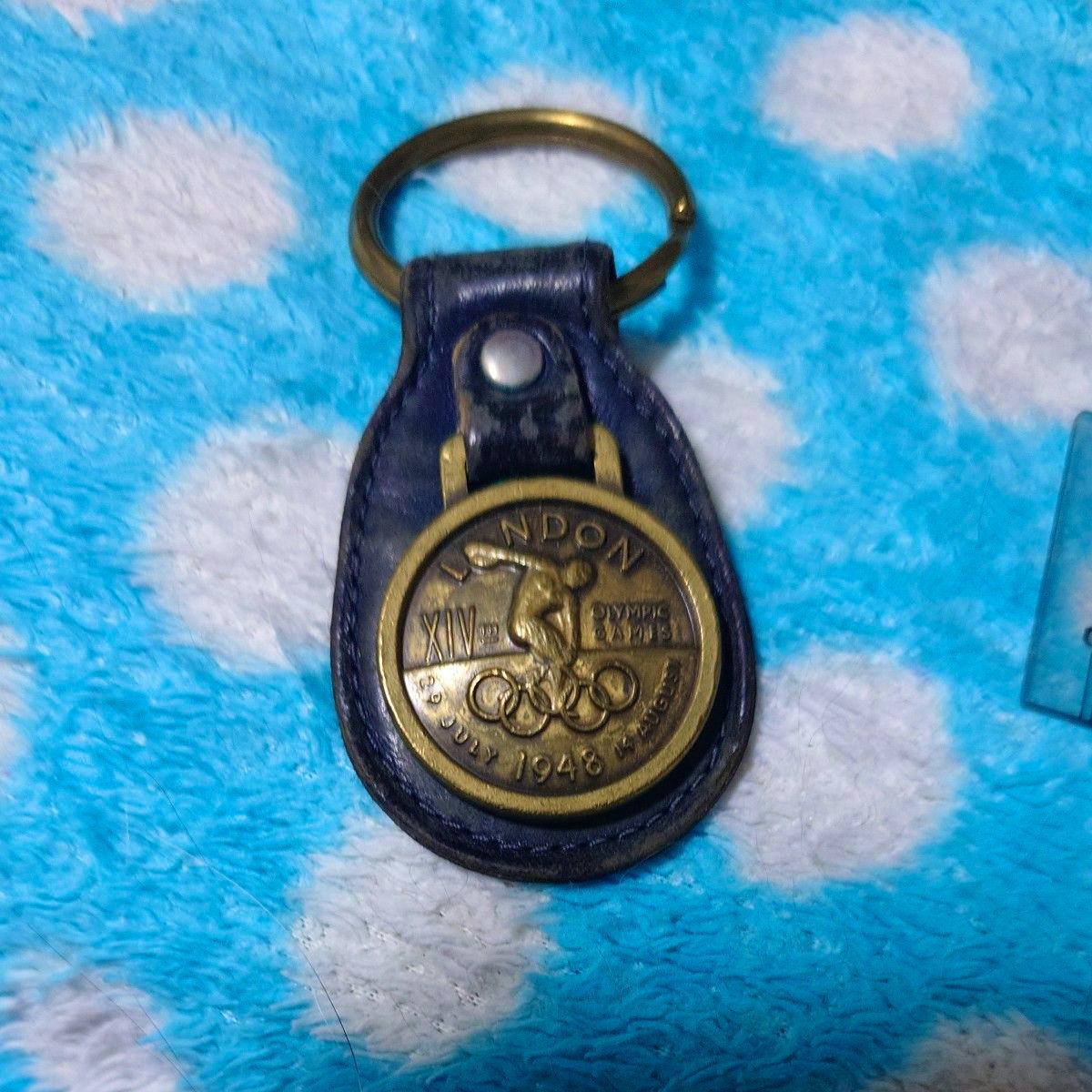 A Coach key holder bag charm with a round bronze-toned medallion mounted on a dark leather fob, shown on a blue polka-dot surface.