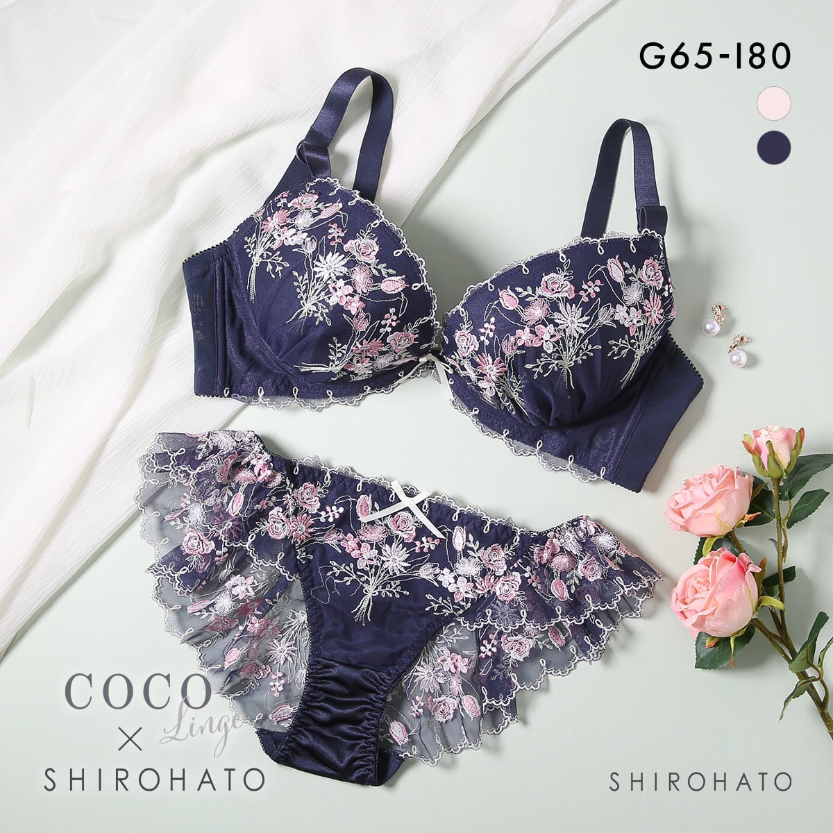 Flat-lay photo of a navy embroidered bra and matching frilly panties displayed on a light background with roses.