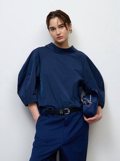 Model wearing the navy cocoon-sleeve pullover with three-quarter sleeves, styled with matching pants and holding a small bag.