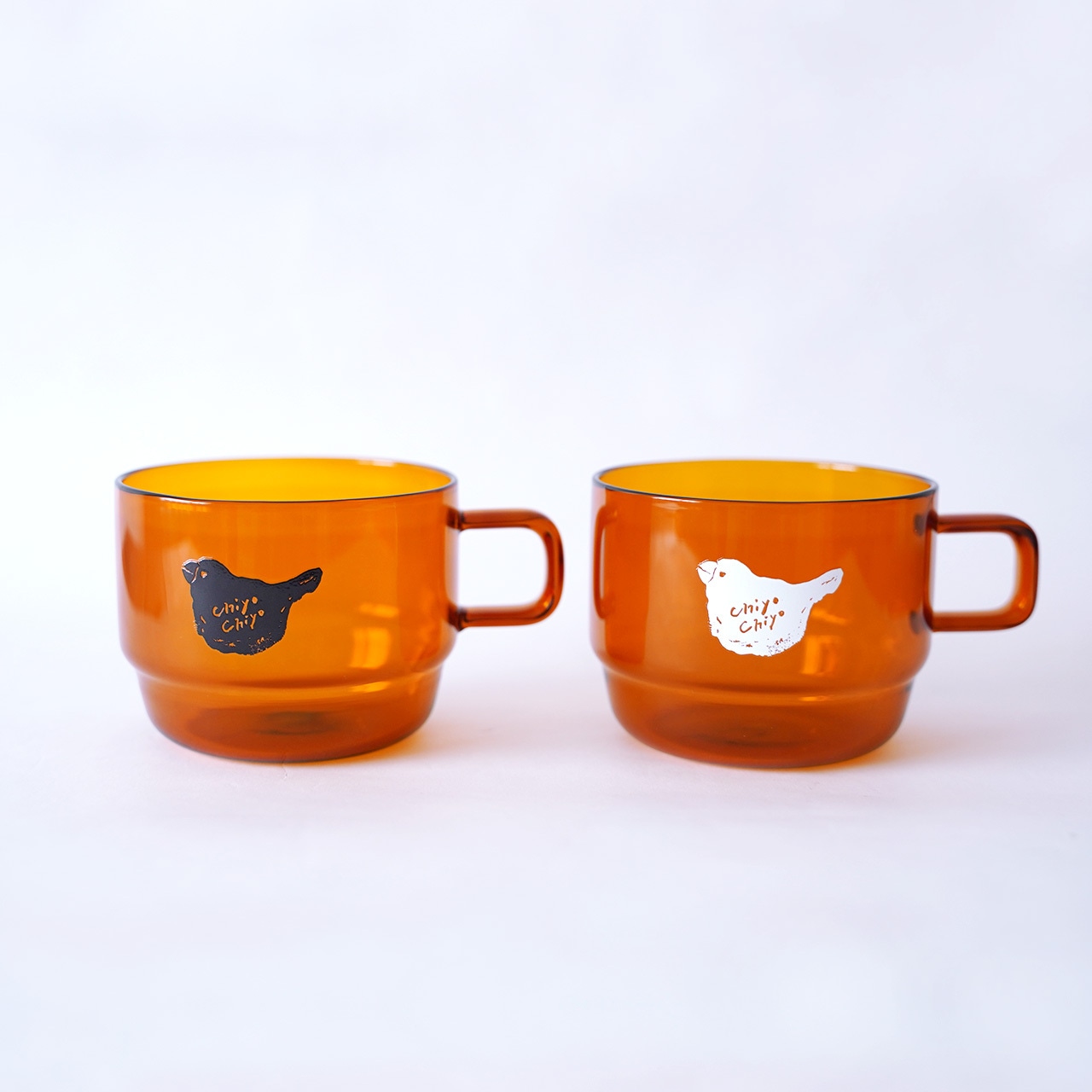 Two amber-colored stack glass mugs with small bird illustrations on the sides shown on a white background.