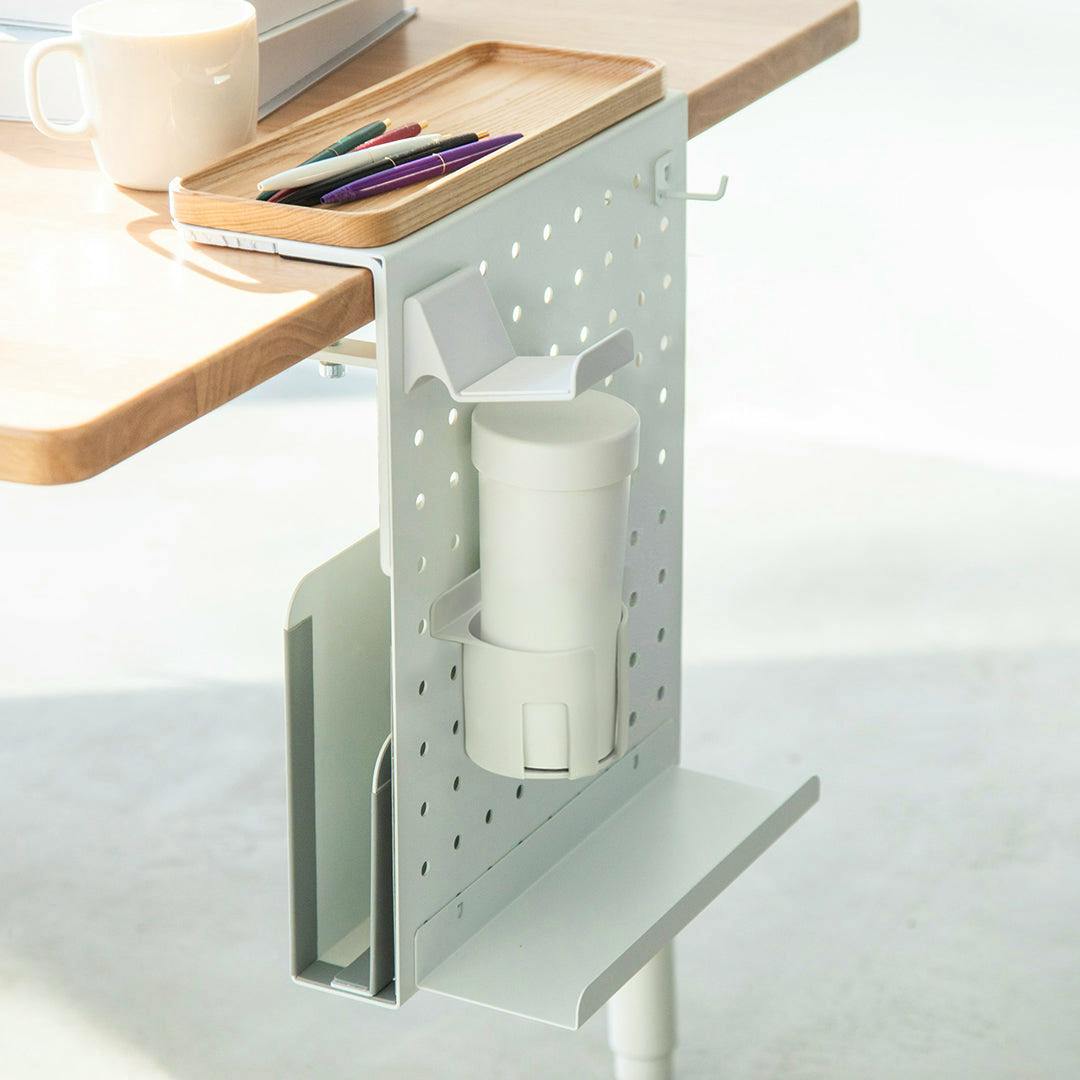 White COFO desk side holder clamped to a table edge with a wooden tray on top holding pens and a cylindrical container attached to the panel.
