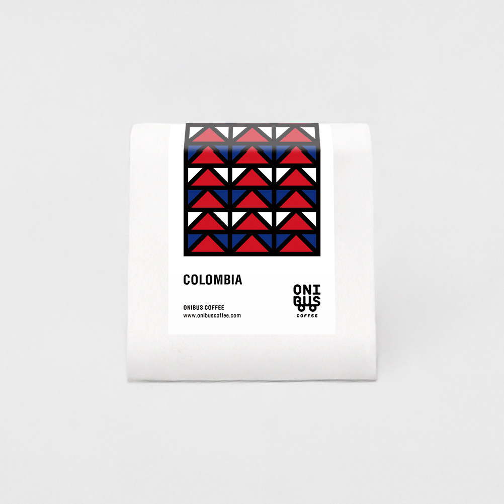 White bag of roasted coffee beans labeled “Colombia” with a red and blue geometric patterned label.