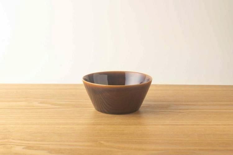 A brown ceramic Colorta bowl with an amber glaze sitting on a wooden surface.