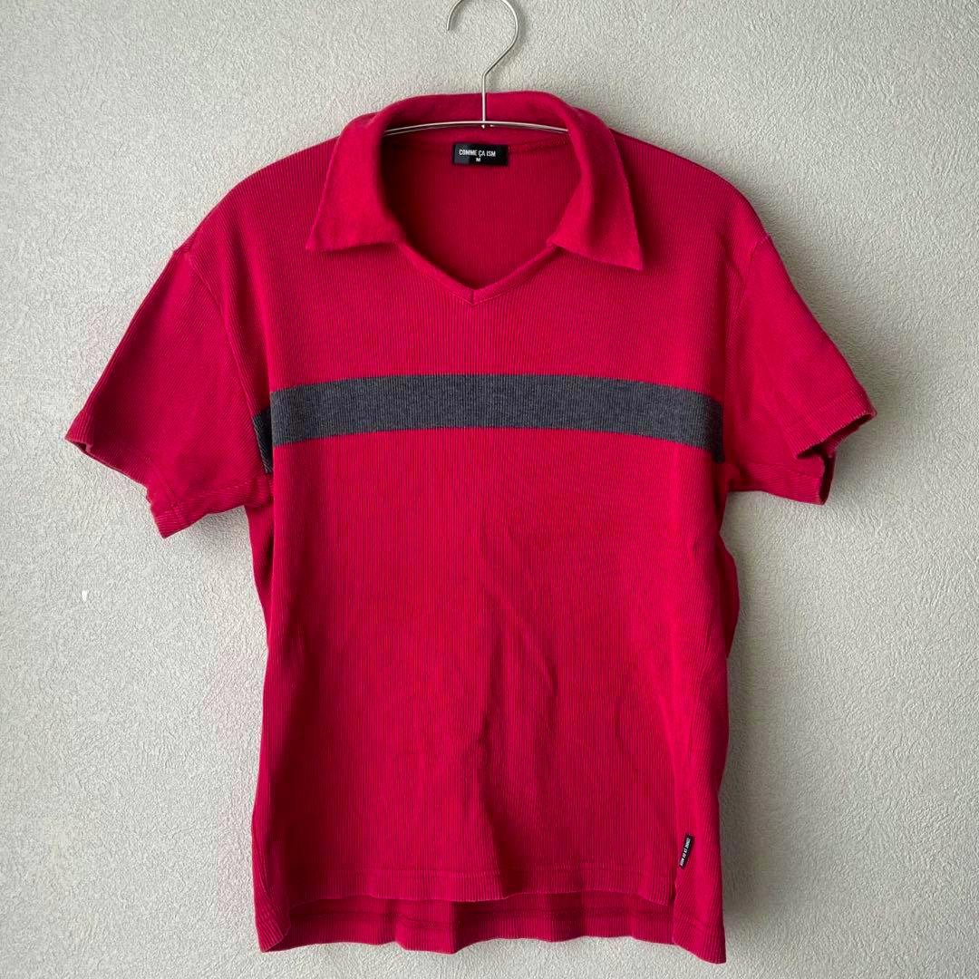 Front view of the red COMME CA ISM short-sleeve polo shirt with a gray horizontal stripe hanging on a metal hanger.