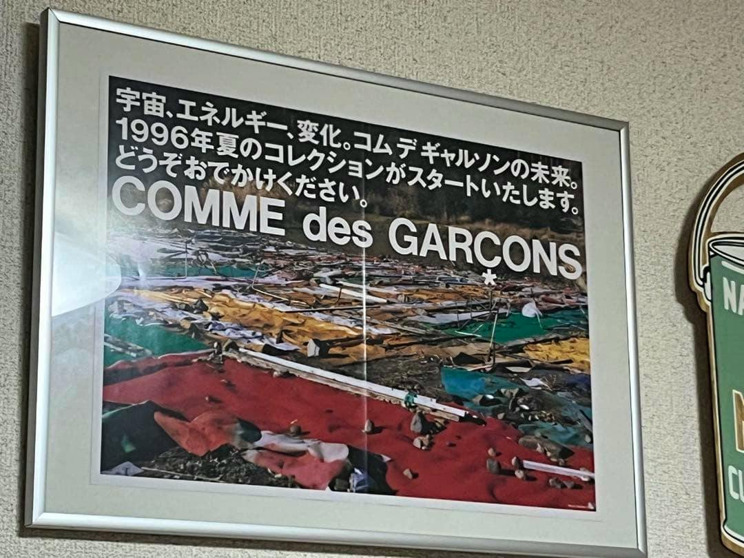 Framed art print showing a COMME des GARÇONS 1996 poster with Japanese text hanging on a wall.