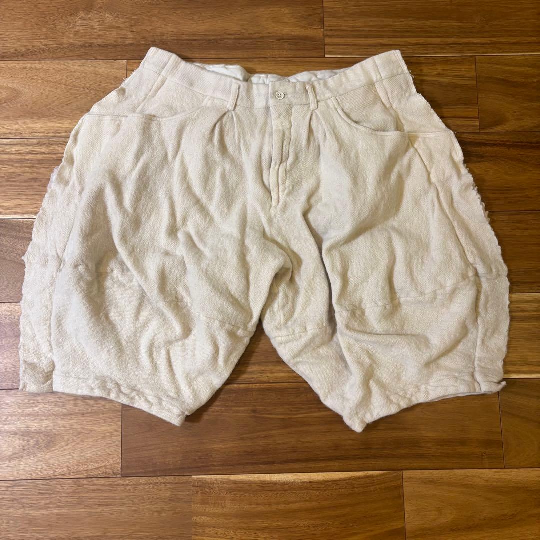 Cream-colored felted wool short pants laid flat on a wooden floor.