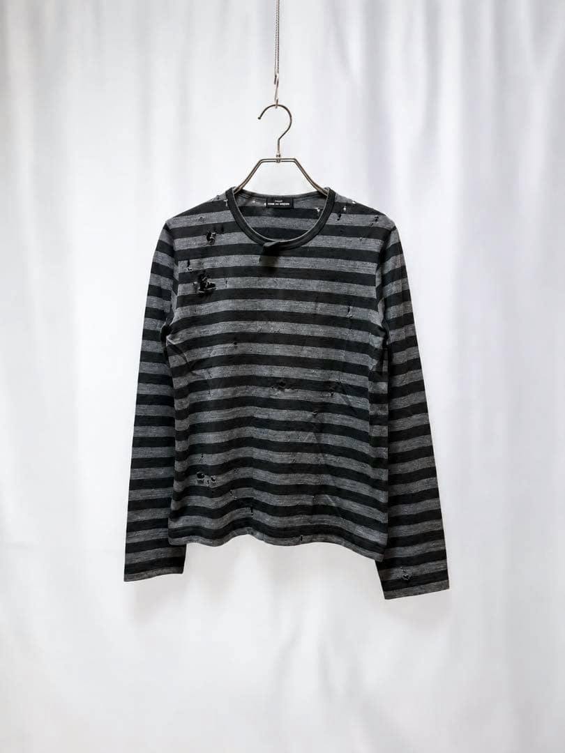A striped long-sleeve distressed knit top hanging on a hanger against a white backdrop.